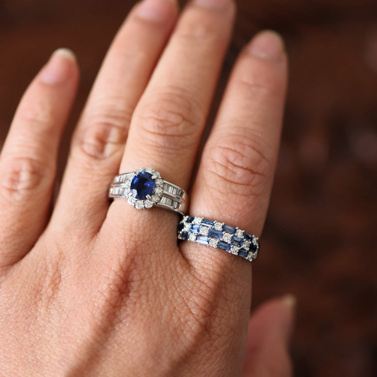 Sapphire and diamond halo ring worn on a finger, paired with a sapphire and diamond half eternity band by emblume