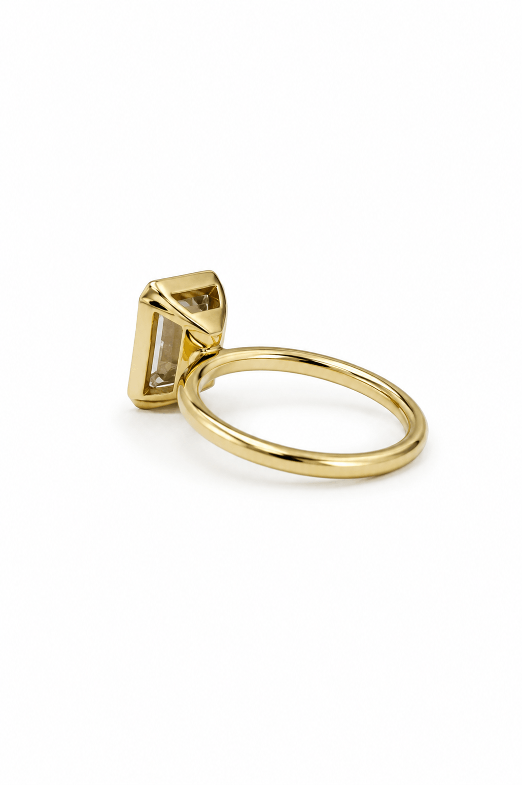 Side view of emerald cut diamond bezel ring in yellow gold showing the raised bezel setting