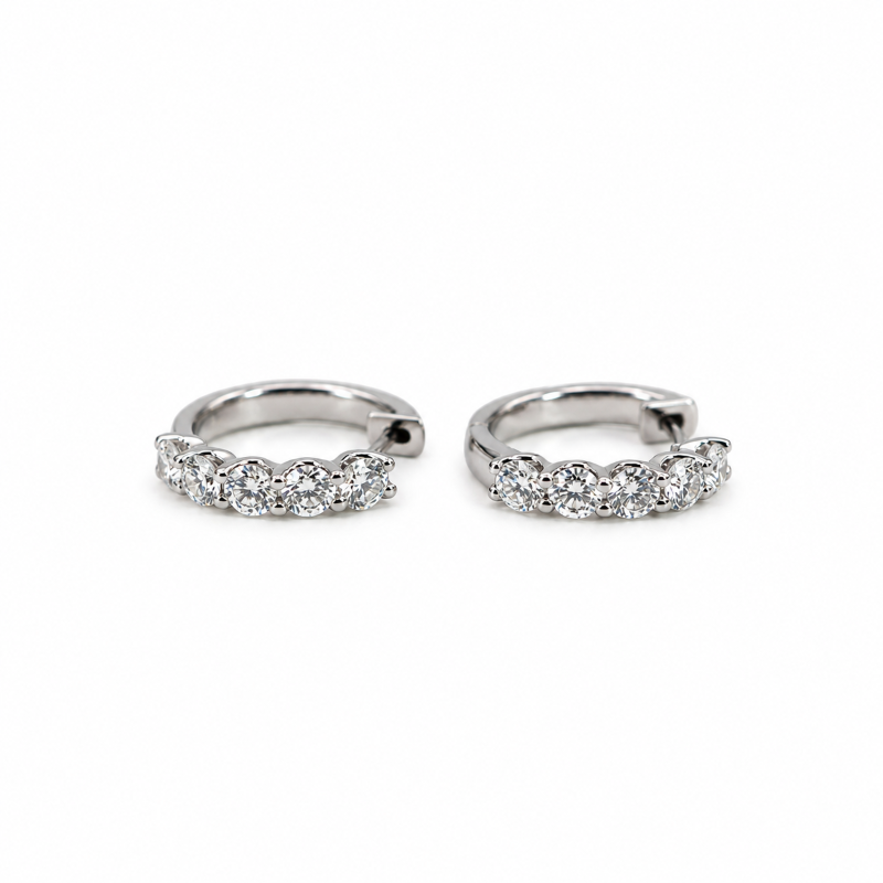 Pair of white gold huggie earrings set with round brilliant-cut diamonds on a white background.