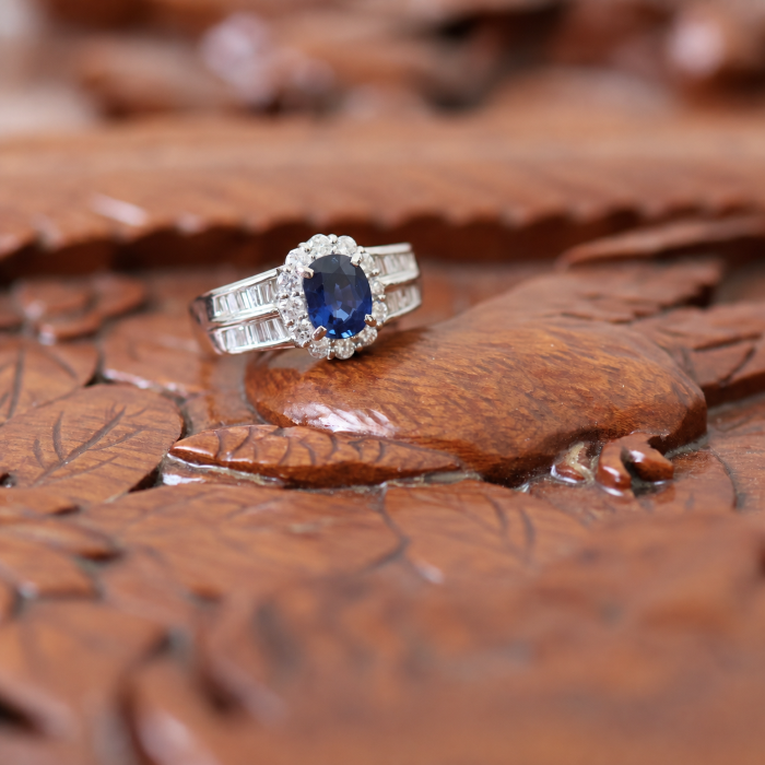 Platinum oval sapphire and diamond halo ring displayed on an antique chinese cabinet by emblume